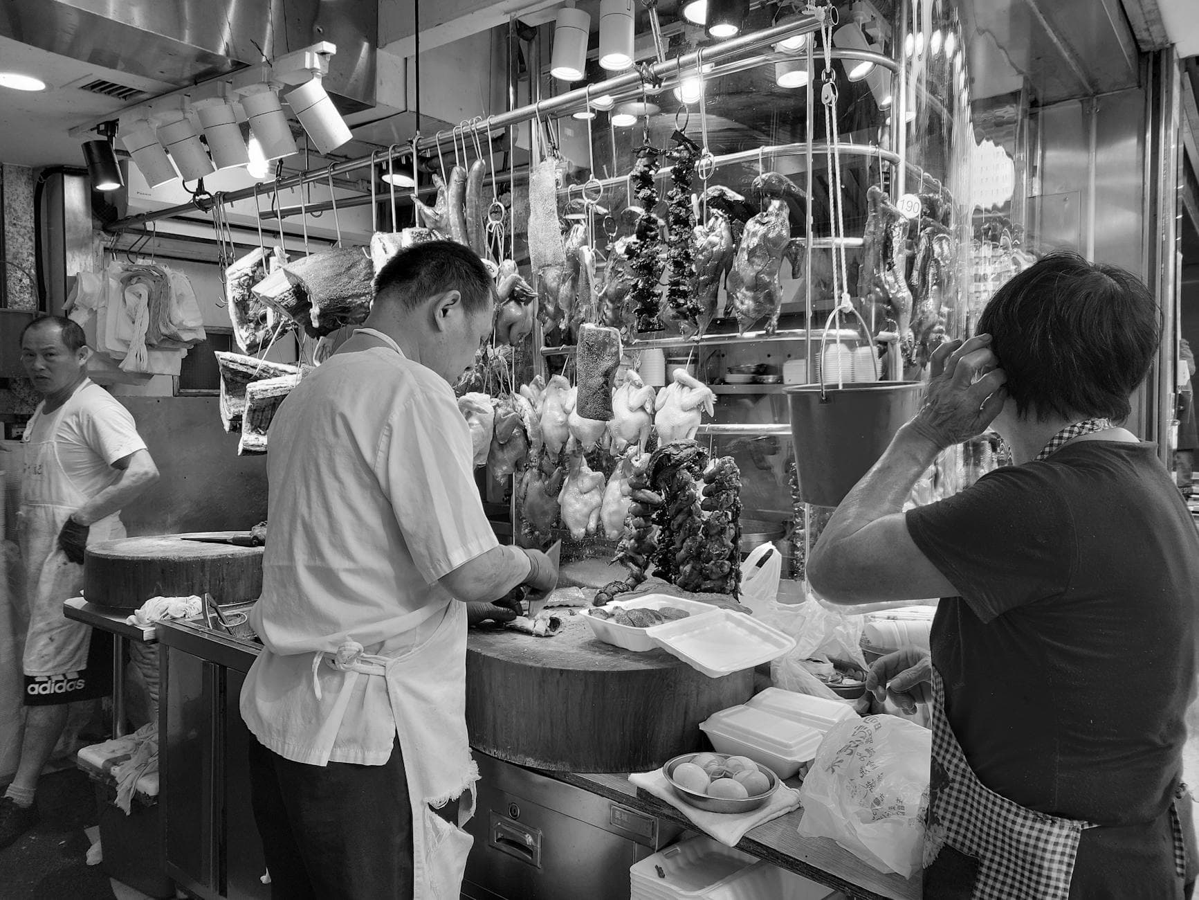 Candid scene of chefs preparing food in a bustling kitchen with hanging meats.
